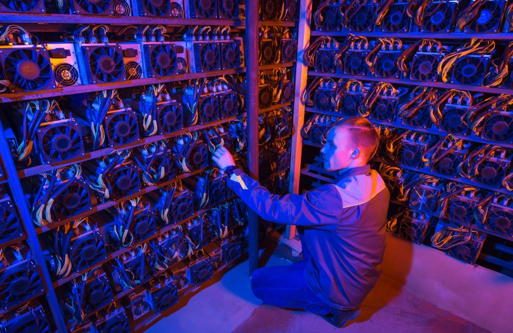 A man in a purple-lit room surrounded by crypto mining rigs