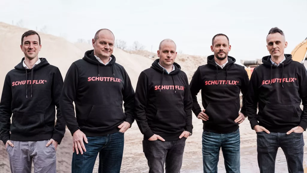 A landscape photo of five male members of the Schüttflix team in black branded hoodies