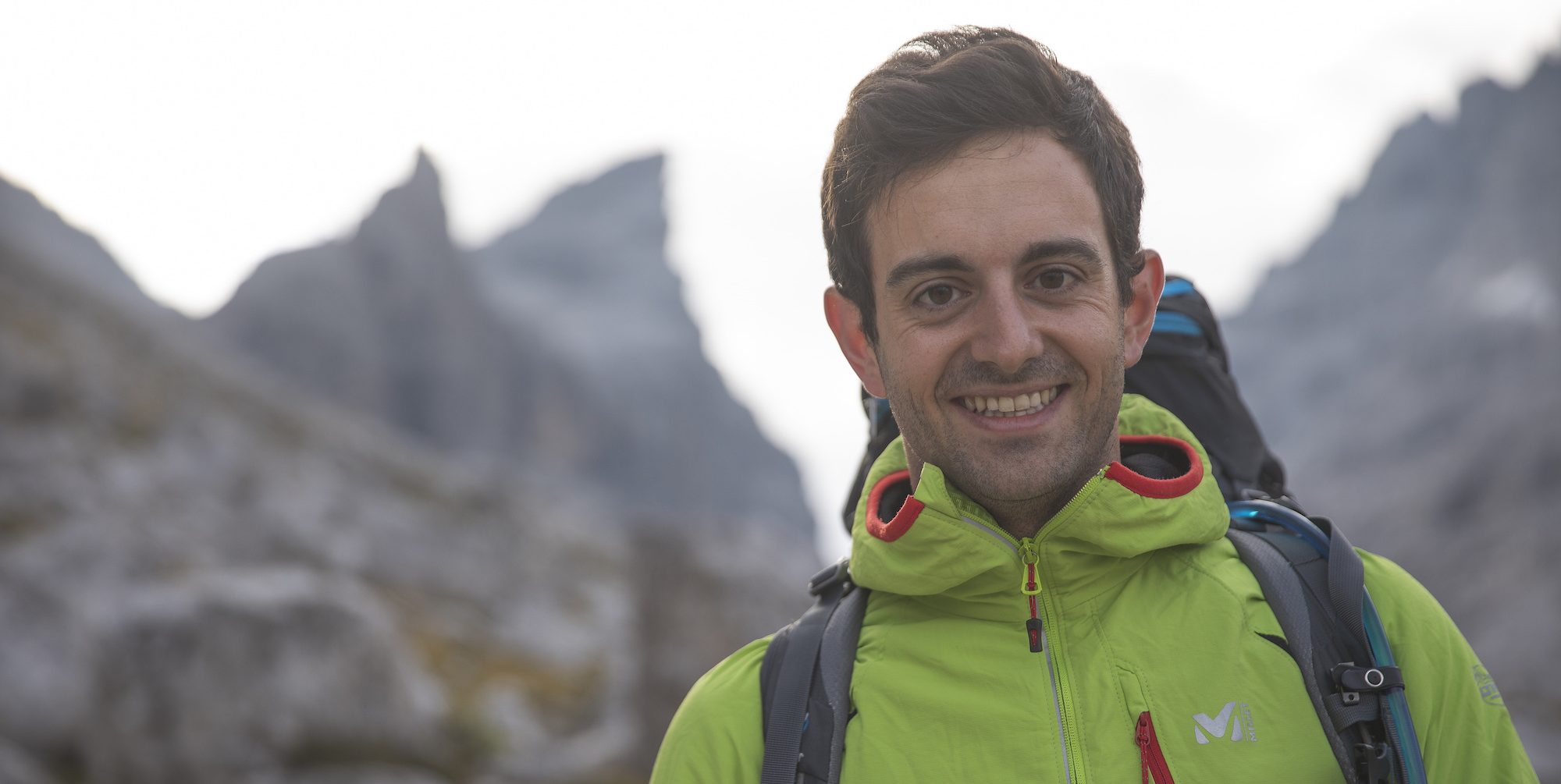 A lansdcape image of Stefano Bernadi in a bright green hiking jacket up a mountain