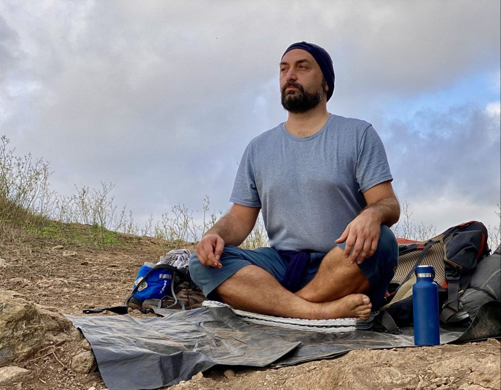 An image of Georgi Karamihaylov sitting cross-legged on a yoga mat on a hill