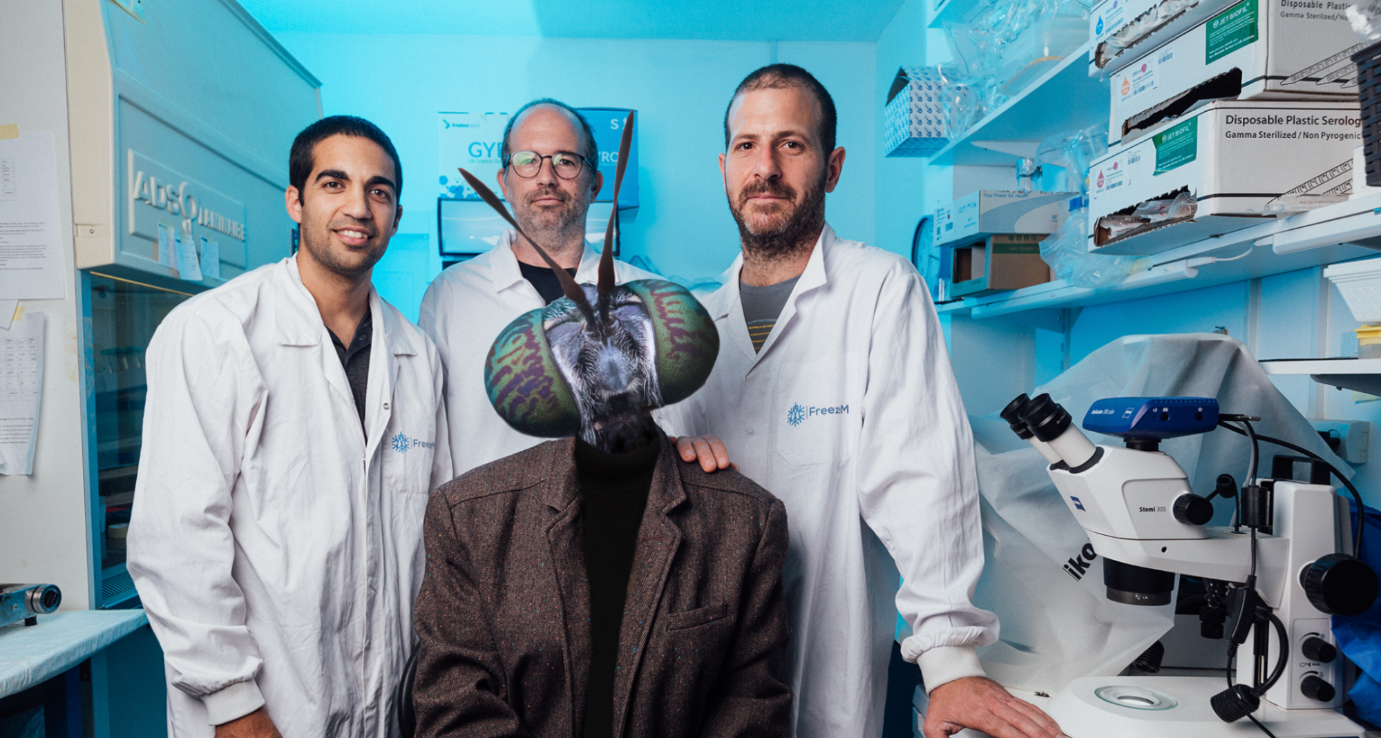 FreezeM. Three cofounders in lab coats stand around a person in a dark coat and a full-size fly mask